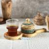 قندان چوبی زبان‌گنجشک با بدنه فیروزه‌کوبی در کنار یک لیوان بلور پر از نوشیدنی چایی قرار گرفته.